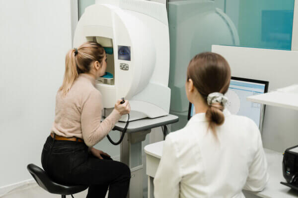 A patient performs a visual field test while an optometrist looks on.